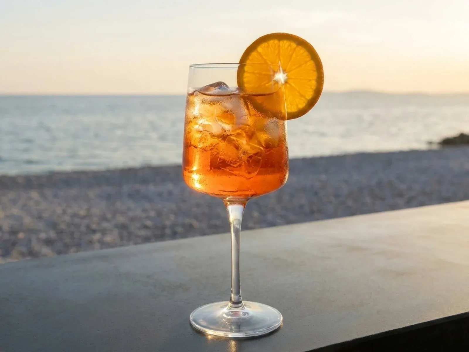 A classic Aperol Spritz with an orange wheel on the rim, on a bar top above the Adriatic at golden hour