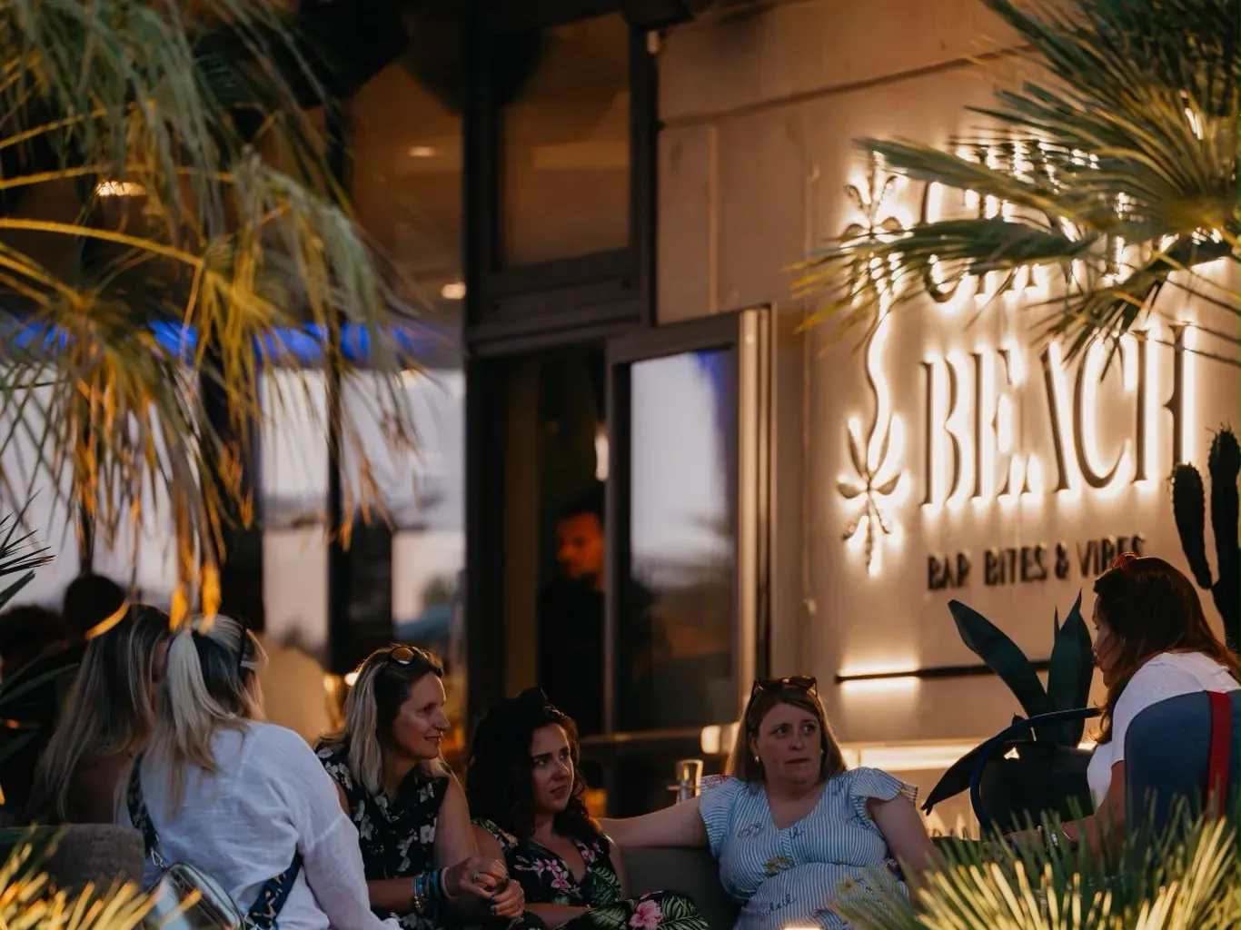 Guests in conversation on the terrace at Central Beach Split under the lit sign, late afternoon