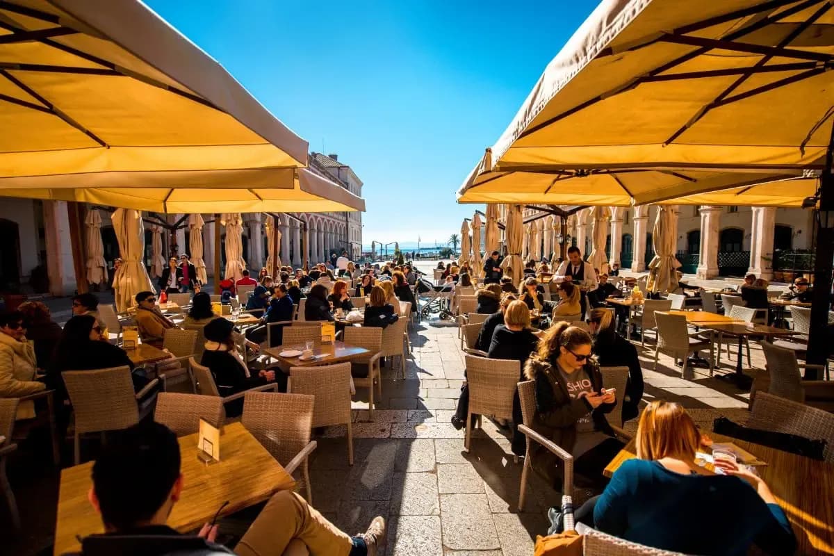 Busy café terraces with yellow parasols on Prokurative square by the sea in Split, Croatia